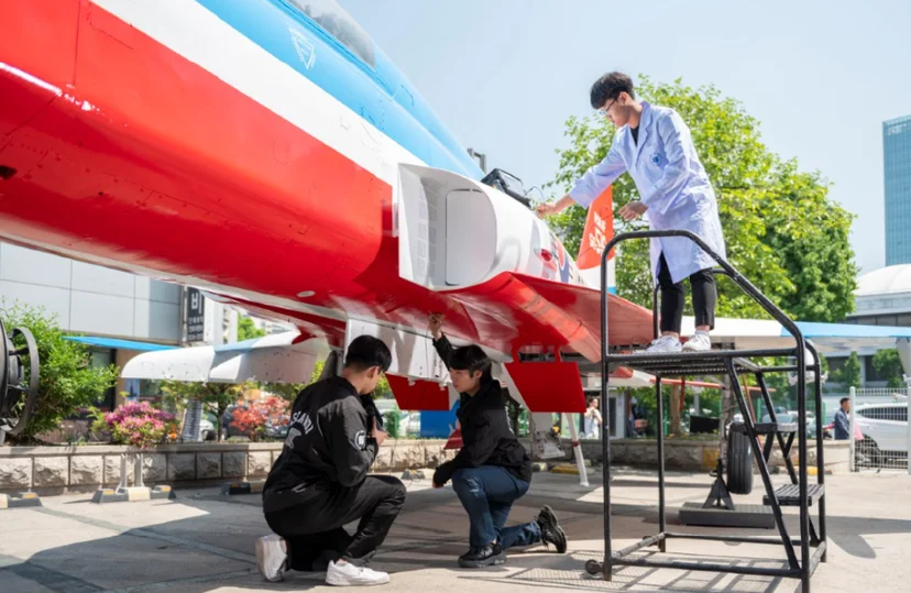 야외 붉고 파란 항공기 옆에서 세 사람이 외판과 아래쪽을 살피고 있는 모습