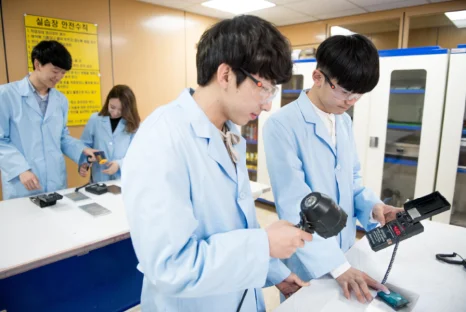 흰 실습복 차림 두 사람이 작업대 위에서 측정 도구를 사용하고 있는 모습