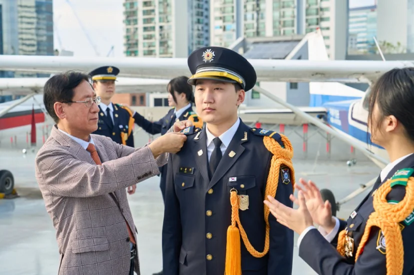 야외 항공기 옆에서 제복 차림 사람의 목 근처를 다른 사람이 만지고 있는 모습