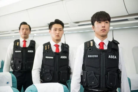 검은 조끼와 붉은 넥타이를 한 세 사람이 항공기 통로에 서 있는 모습