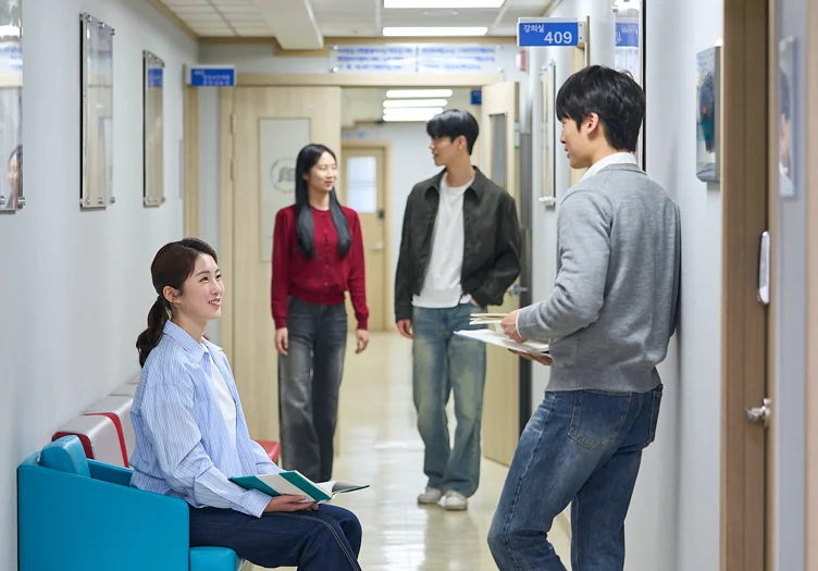 복도에서 푸른 작업복 차림 앉은 사람과 붉은 상의 차림 사람 등 네 사람이 이야기하고 있는 모습