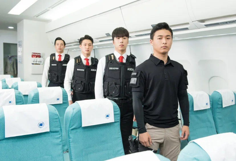 항공기 객실 모양 좌석 사이에 검은 조끼와 정장을 입은 네 사람이 서 있는 모습
