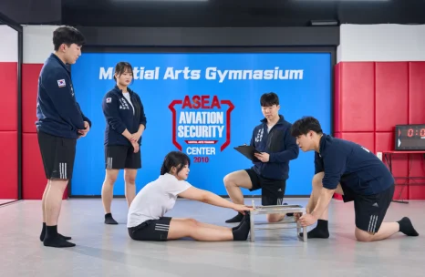 매트에 앉은 사람의 발을 앞에 무릎 꿇은 사람이 잡고 여러 사람이 주위에서 보고 있는 모습