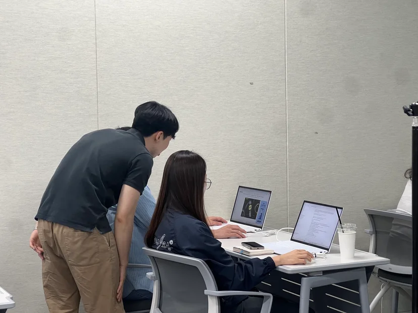 AI 기초 과정 실습 시간에 보조강사가 수강생 옆에서 화면을 함께 보며 지원하는 장면