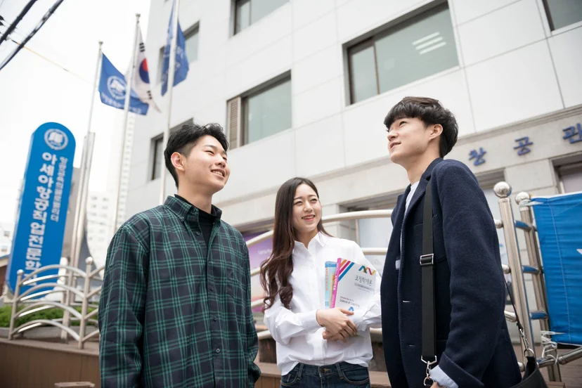 학교 건물 앞에서 책자를 들고 이야기하는 학생들