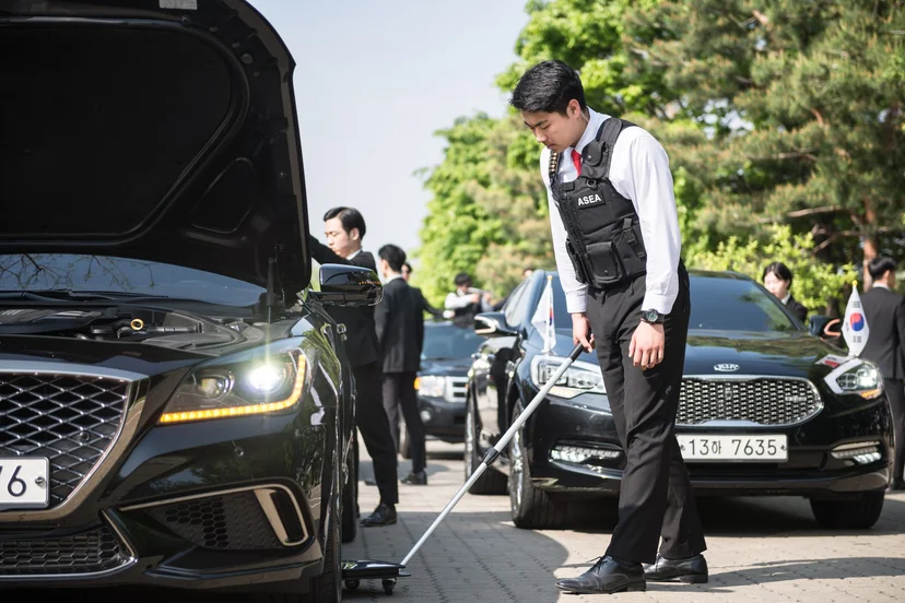 차량 옆에서 긴 거울로 차체 아래를 살펴보는 모습
