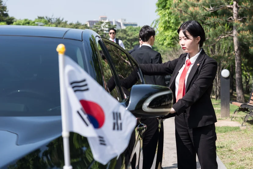 태극기가 달린 검은 승용차의 문을 열고 있는 정장 차림 학생