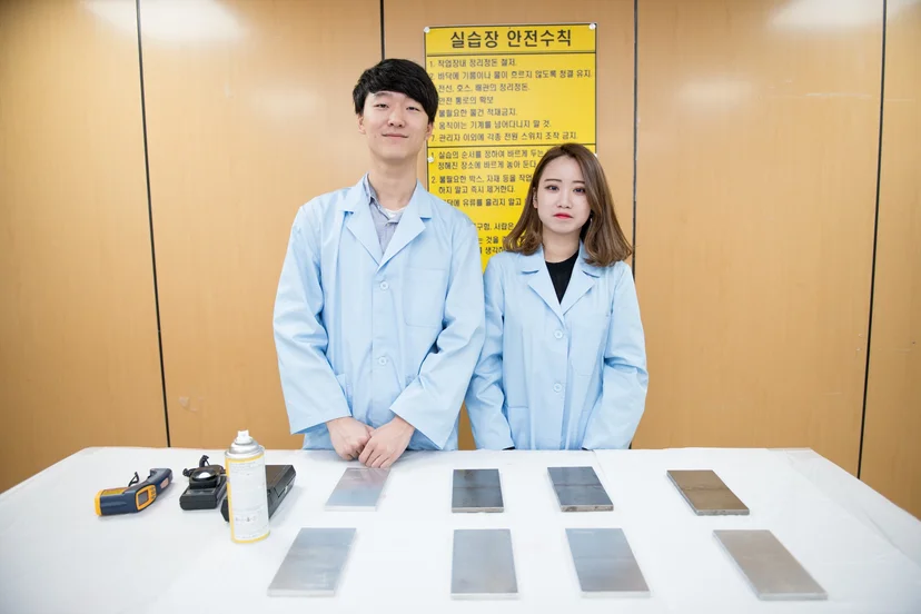 여러 금속 시편과 측정 도구가 놓인 책상 뒤에 서 있는 사람들