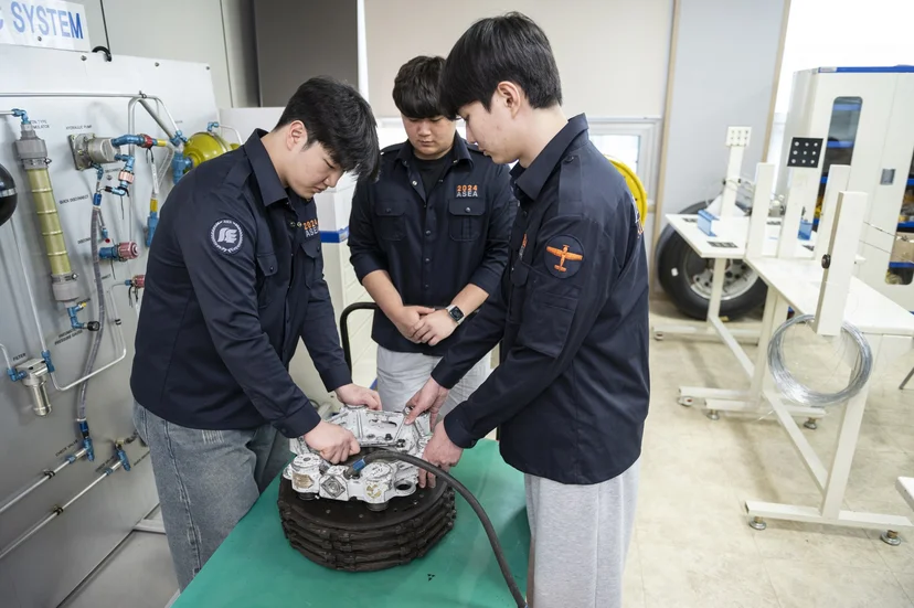 실습대 위 엔진 실린더를 함께 다루는 학생들