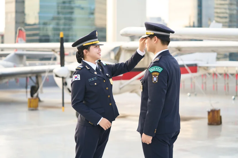 항공기 앞에서 서로의 모자와 복장을 점검하는 두 학생