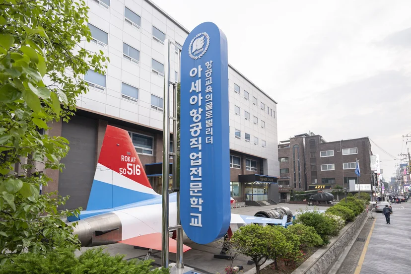 학교 건물 앞 간판과 전시된 항공기 꼬리날개