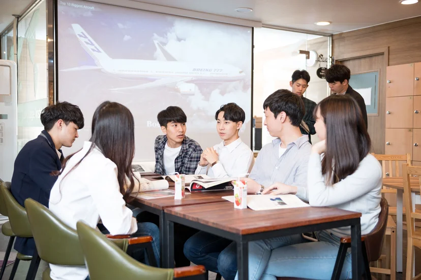 스크린 앞 테이블에 모여 이야기를 나누는 학생들