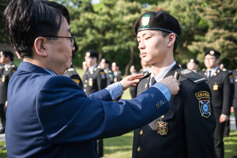야외 행사에서 제복 차림 학생의 가슴에 표식을 달아 주는 모습