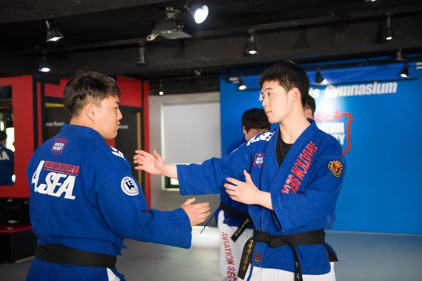 파란 도복을 입은 두 학생이 매트 위에서 잡기 동작을 연습하는 모습