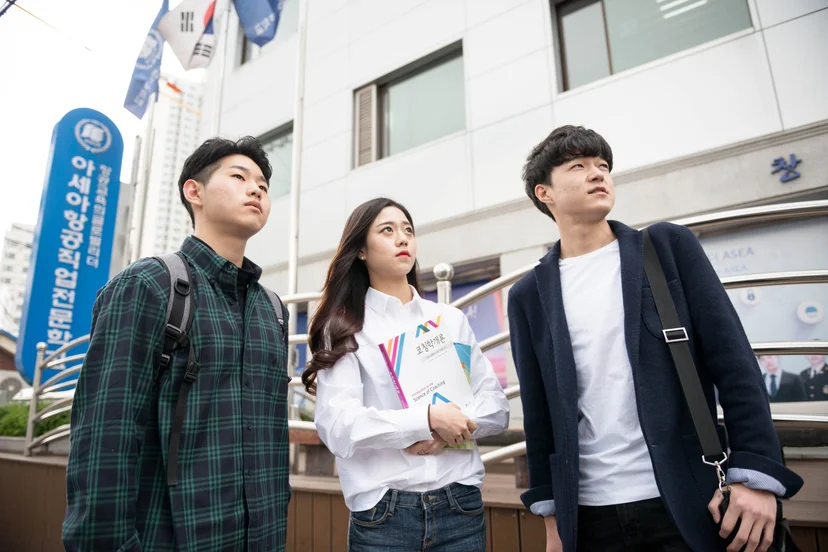 학교 건물 앞에서 자료를 들고 주변을 살펴보는 사람들