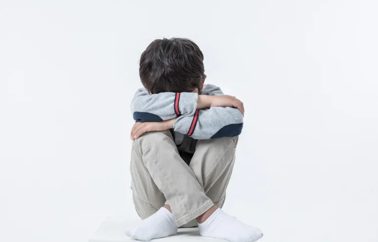 무릎을 안고 고개를 숙인 채 앉아 있는 아이