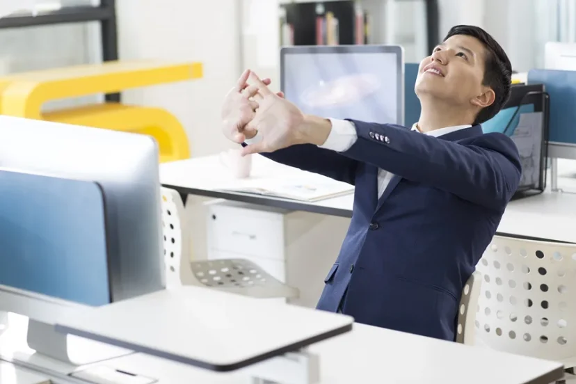 사무실 책상에 앉아 기지개를 켜며 스트레칭하는 직장인