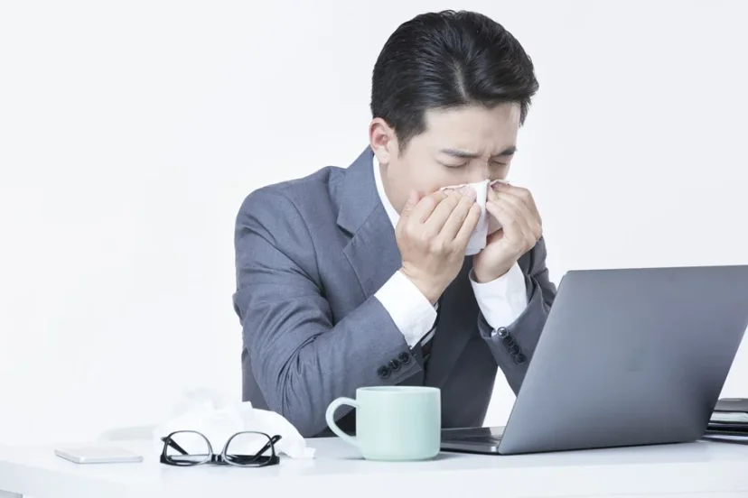 사무실에서 코를 풀며 괴로워하는 감기 걸린 직장인