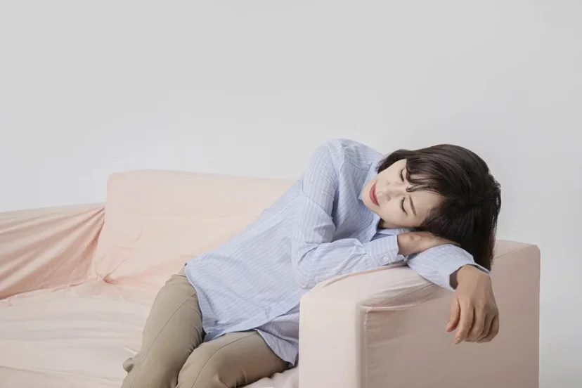 소파에 기대어 피로와 통증을 느끼는 여성