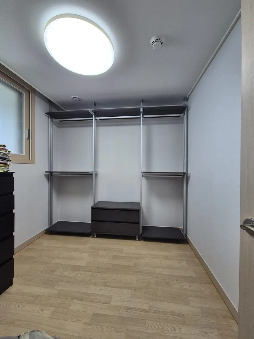 일자형 드레스룸 정면. 다크스톤 색 상부 옷봉과 중단 선반, 하부 서랍장으로 구성. 실버 기둥 3개. 밝은 목재 바닥.