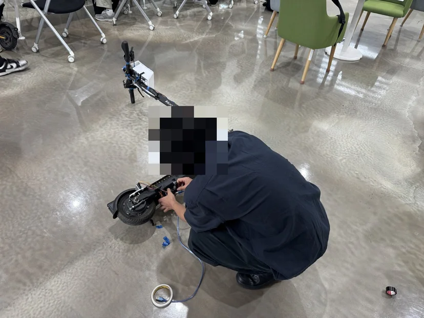 바닥에 눕힌 킥보드의 배선을 연결하는 학생