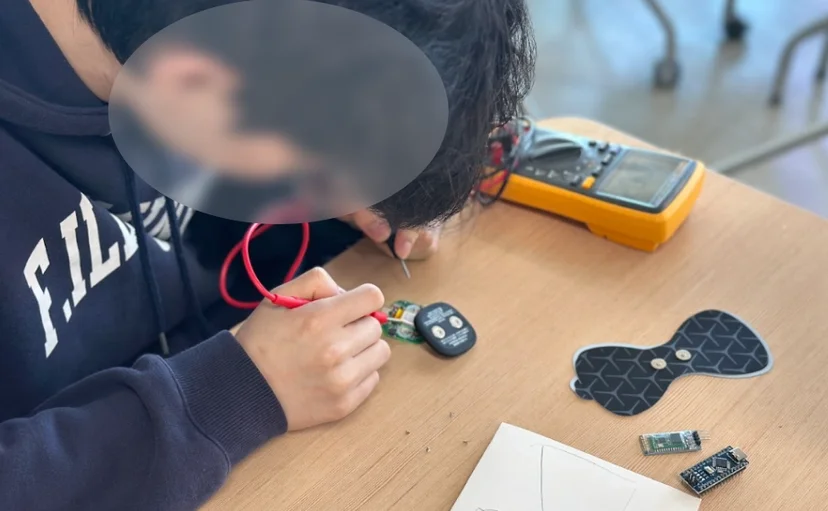 나비 모양 패드가 달린 헬스케어 기기를 분해해 멀티미터로 회로를 확인하는 학생