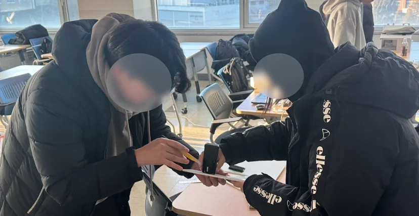 기기를 종이 위에 올리고 자와 연필로 치수를 재는 학생들
