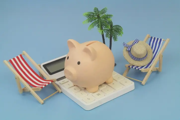 계산기 위에 돼지 저금통이 올려져 있고 그 양옆에는 비치 체어 모형이 놓여있는 모습