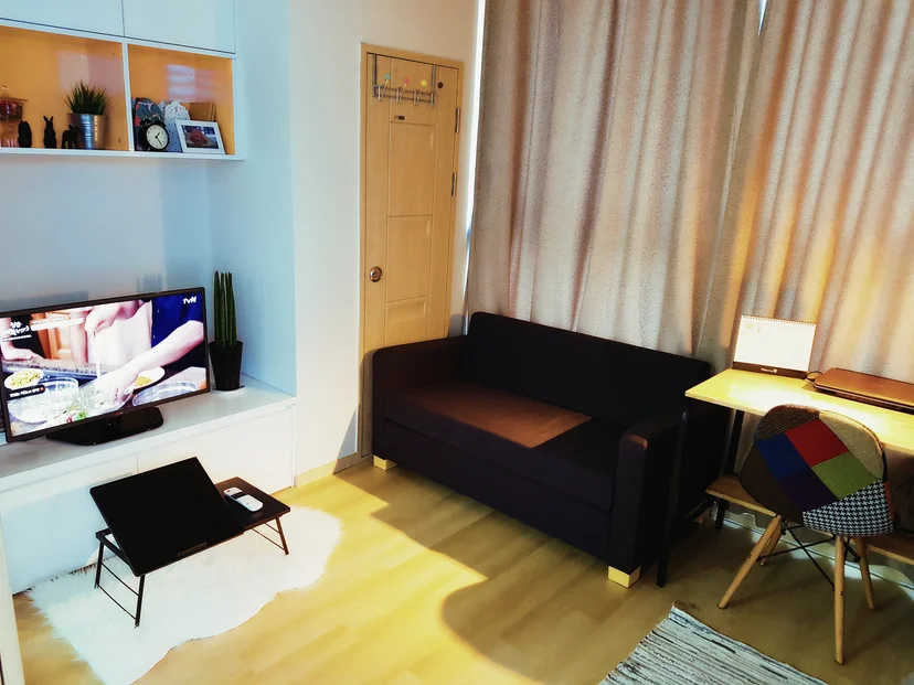 Living area with a navy sofa, a wall-mounted TV and a desk with a colorful chair (Listing ID : 25)
