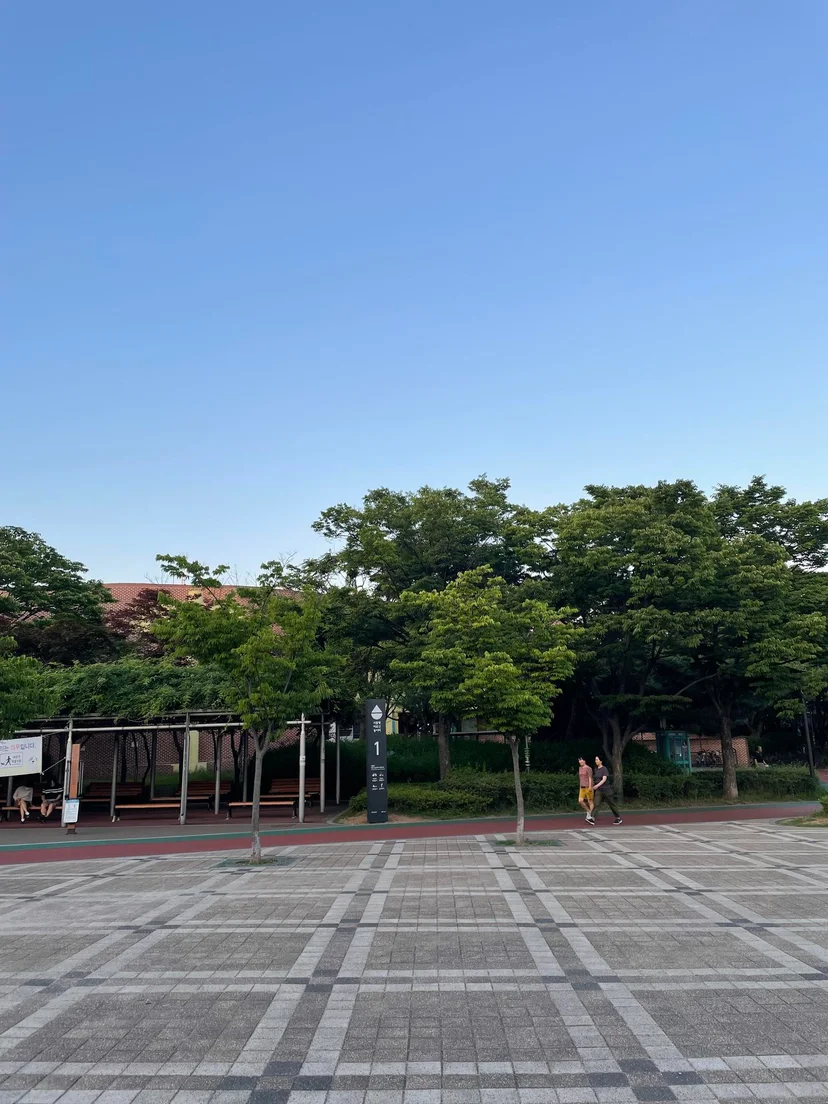 Park plaza with a wide paved walkway, young trees and a shaded pergola (Listing ID : 17562)
