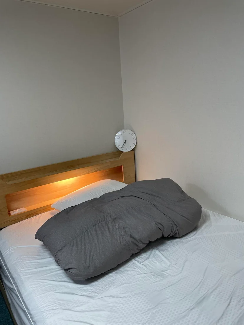 Bed with a wooden headboard, reading light and a wall clock above it (Listing ID : 17562)