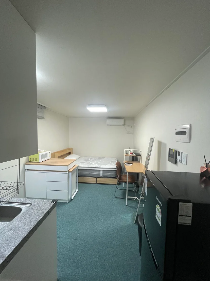 Studio room seen from the kitchen end, with a bed, a small desk and a wall air conditioner (Listing ID : 17562)