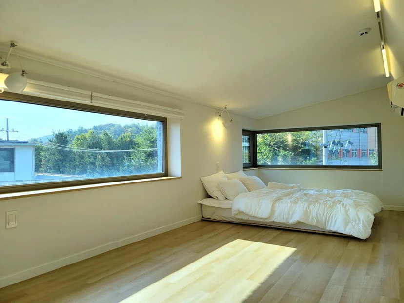 Sunlit bedroom with wide windows and a green hillside view (Listing ID : 17400)