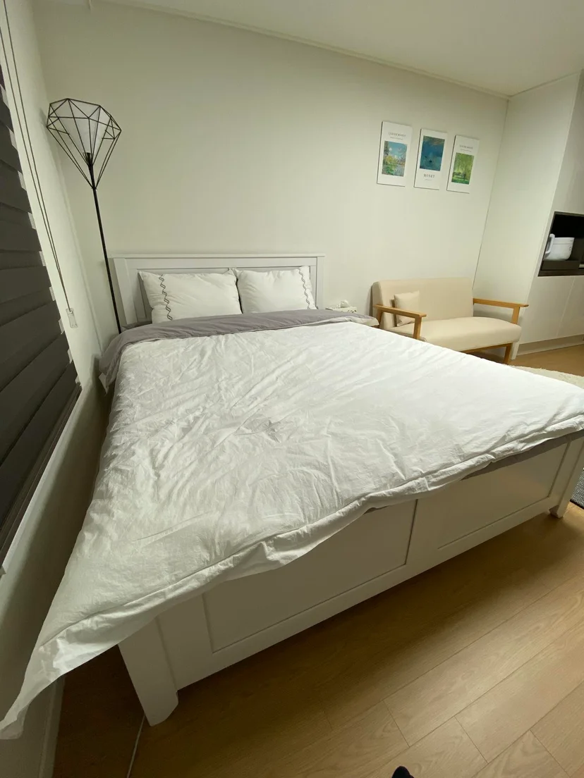 Studio bedroom with white-framed bed and geometric floor lamp (Listing ID : 17787)