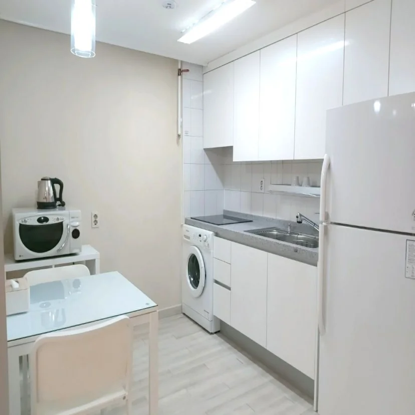 White kitchen with fridge, induction cooktop, washer, and compact glass dining table (Listing ID : 34007)