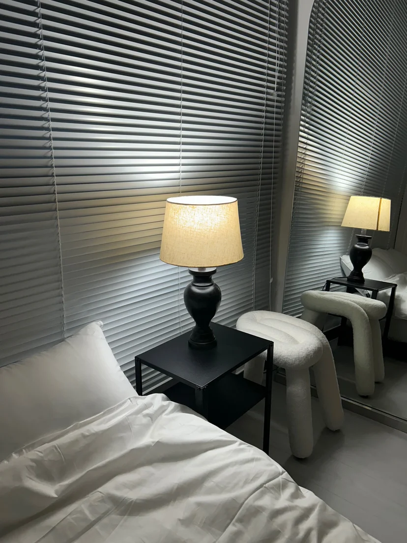 Bed corner with a nightstand lamp, mirror, and small stool (Listing ID : 30632)