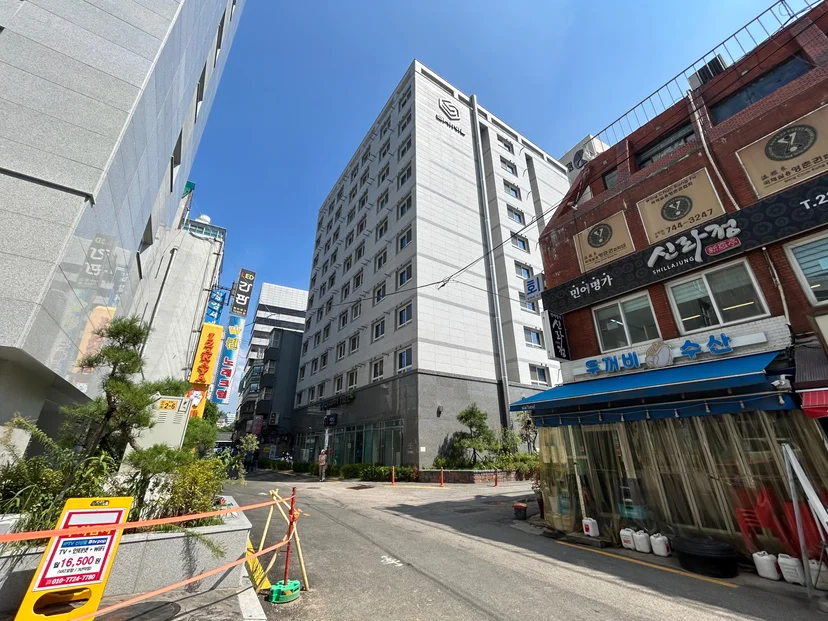 Street-level view of the white officetel building among local shops (Listing ID : 30036)