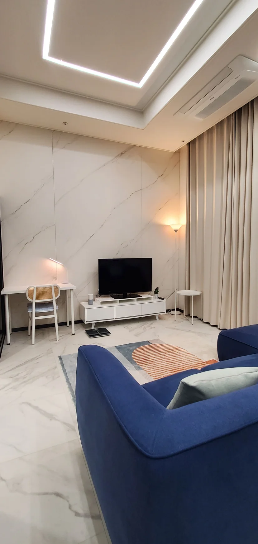 Living room with a blue sofa, TV and marble accent wall (Listing ID : 26402)