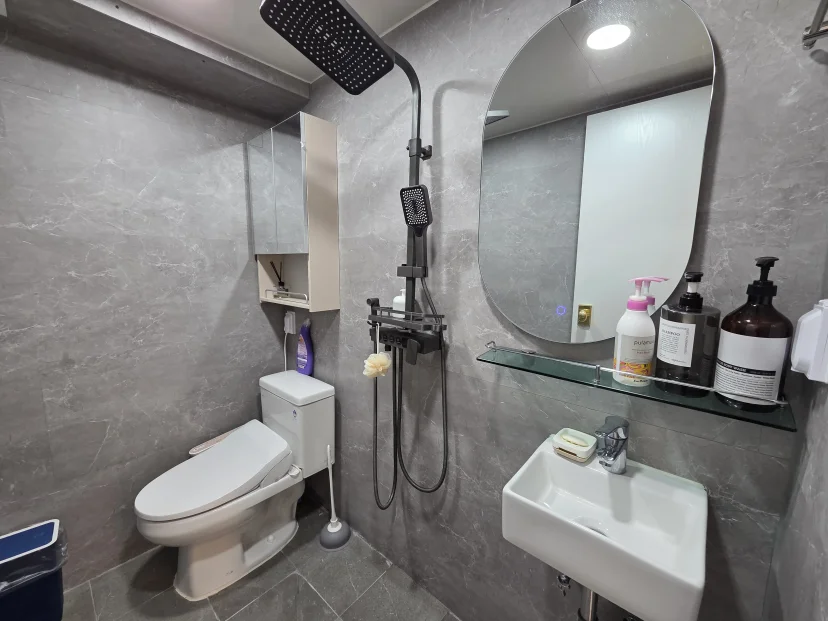 Grey-tiled bathroom with rainfall shower, toilet, oval mirror, and wall-mounted sink (Listing ID : 43593)