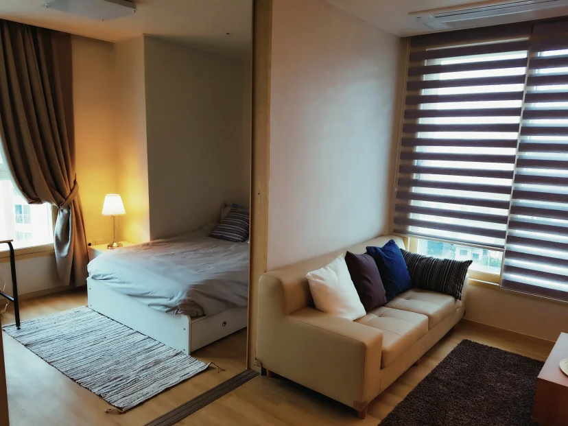 Studio space with a sofa by the window and a double bed set behind a partition (Listing ID : 25)