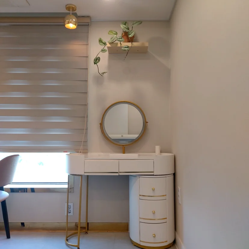White vanity desk with round mirror and gold accents by zebra-blind window (Listing ID : 43593)
