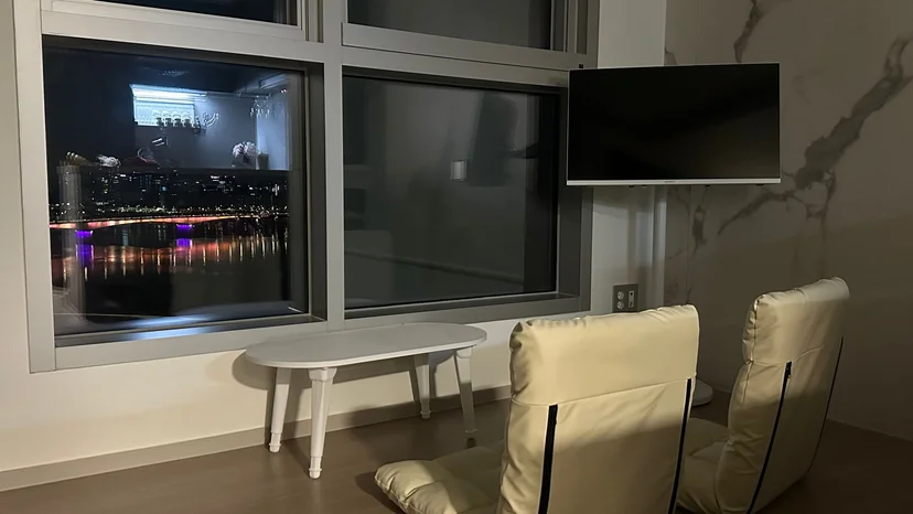 Living area with a wall-mounted TV, floor cushion seating and a night river view (Listing ID : 32655)