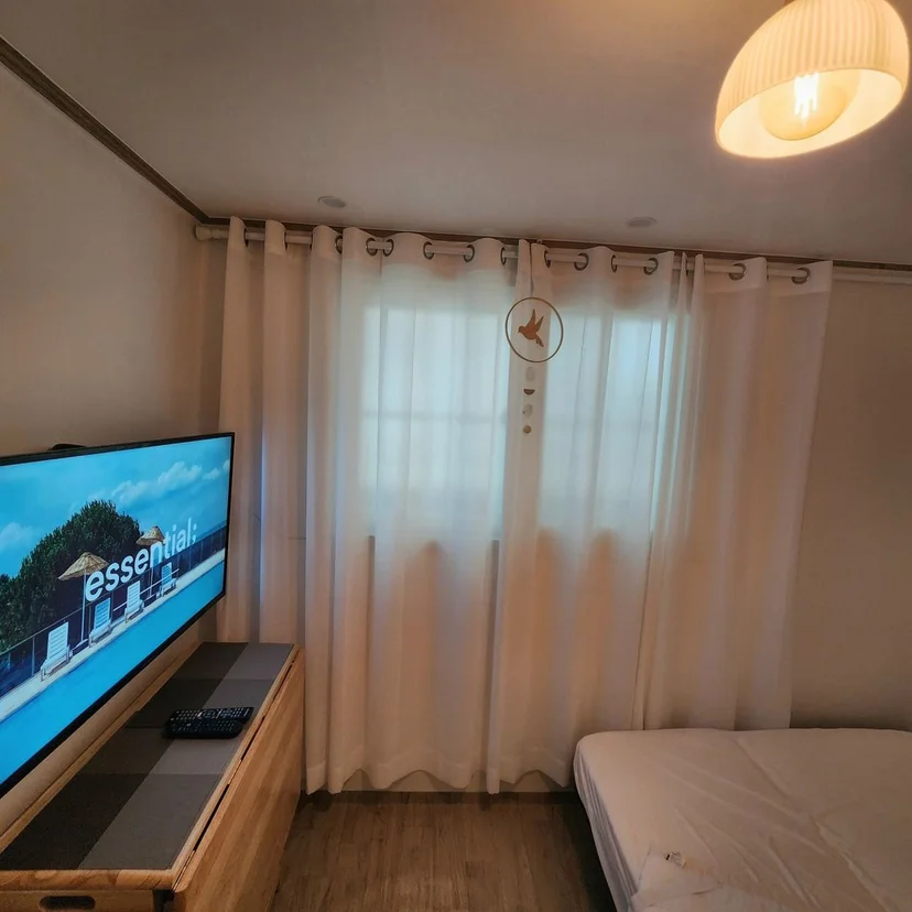 Second room with a wall-mounted TV, wood console, and sheer curtains (Listing ID : 25853)