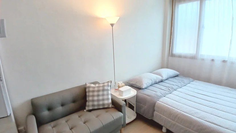 Studio room with a bed, sofa, and floor lamp beside the window (Listing ID : 28802)