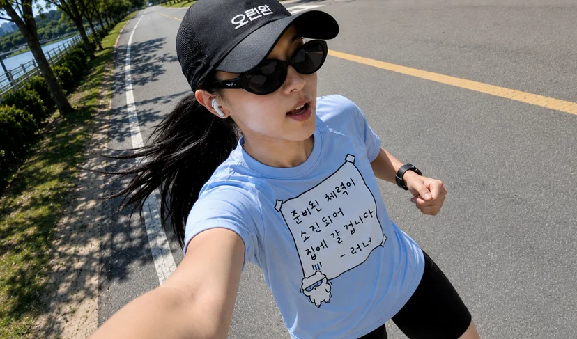 마플 러닝 크루 굿즈 – 오런완 문구를 인쇄한 검은색 러닝 볼캡과 응원 문구를 넣은 하늘색 기능성 티셔츠를 착용하고 야외에서 달리는 여성 이미지