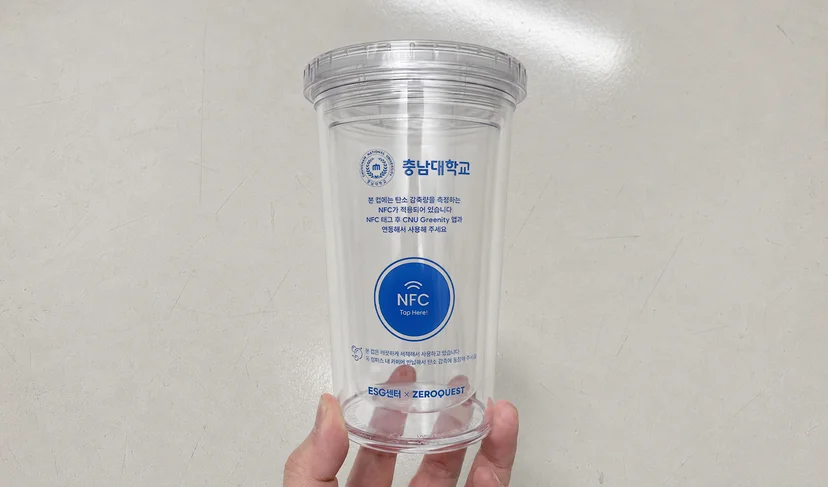 마플 NFC 리유저블컵 – 투명 컵 전면에 충남대학교 로고와 NFC 태그 안내 문구를 파란색으로 인쇄해 회색 바닥에 놓은 이미지