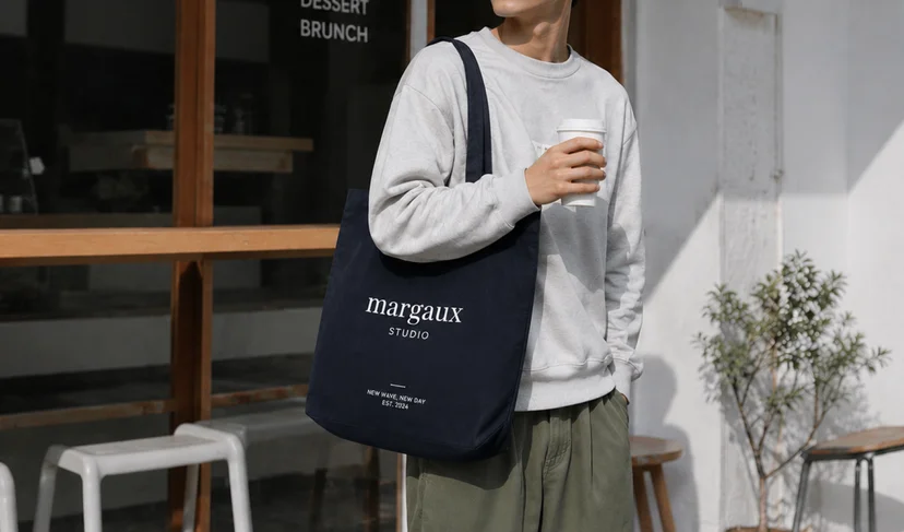 브랜드 로고가 인쇄된 네이비 색상의 마플 스탠다드 캔버스 에코백을 남성이 착용한 이미지