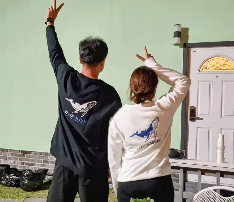 마플 커플 맨투맨 제작 – 고래 일러스트와 레터링을 등판에 프린팅한 블랙과 화이트 맨투맨을 맞춰 입은 두 사람의 뒷모습 이미지